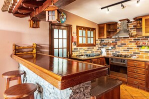 A kitchen with a stone island, wooden bar stools, a brick backsplash, and wooden cabinets.