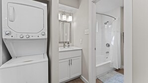 A modern bathroom with a built-in washer and dryer, a vanity with a mirror, and a walk-in shower. - Stylish Modern Studio Close to Downtown and Domain (Austin)