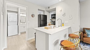 A modern kitchen with white cabinetry, a central island, and bar stools. - Stylish Modern Studio Close to Downtown and Domain (Austin)