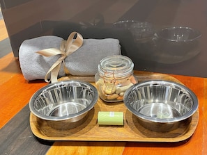 A wooden tray with two metal bowls, a jar of snacks, a gift-wrapped item, and a grey cushion. - Pam's House (Weymouth)