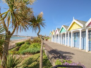 A row of colorful beach huts with a beach and ocean in the background. - Pam's House (Weymouth)