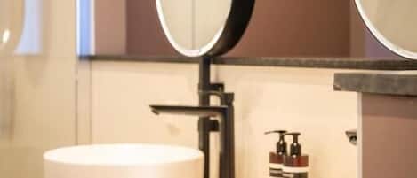 Une salle de bain moderne avec deux vasques rondes blanches, un grand miroir et un porte-serviettes.