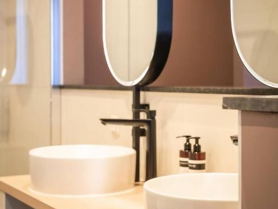 Une salle de bain moderne avec deux vasques rondes blanches, un grand miroir et un porte-serviettes.
