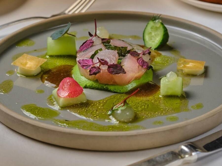 Een bord eten met een stuk vlees in het midden, omringd door verschillende groenten en garneringen.