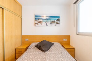 A bedroom with a bed, a wooden headboard, a nightstand, a drawer, and a painting of a beach scene.