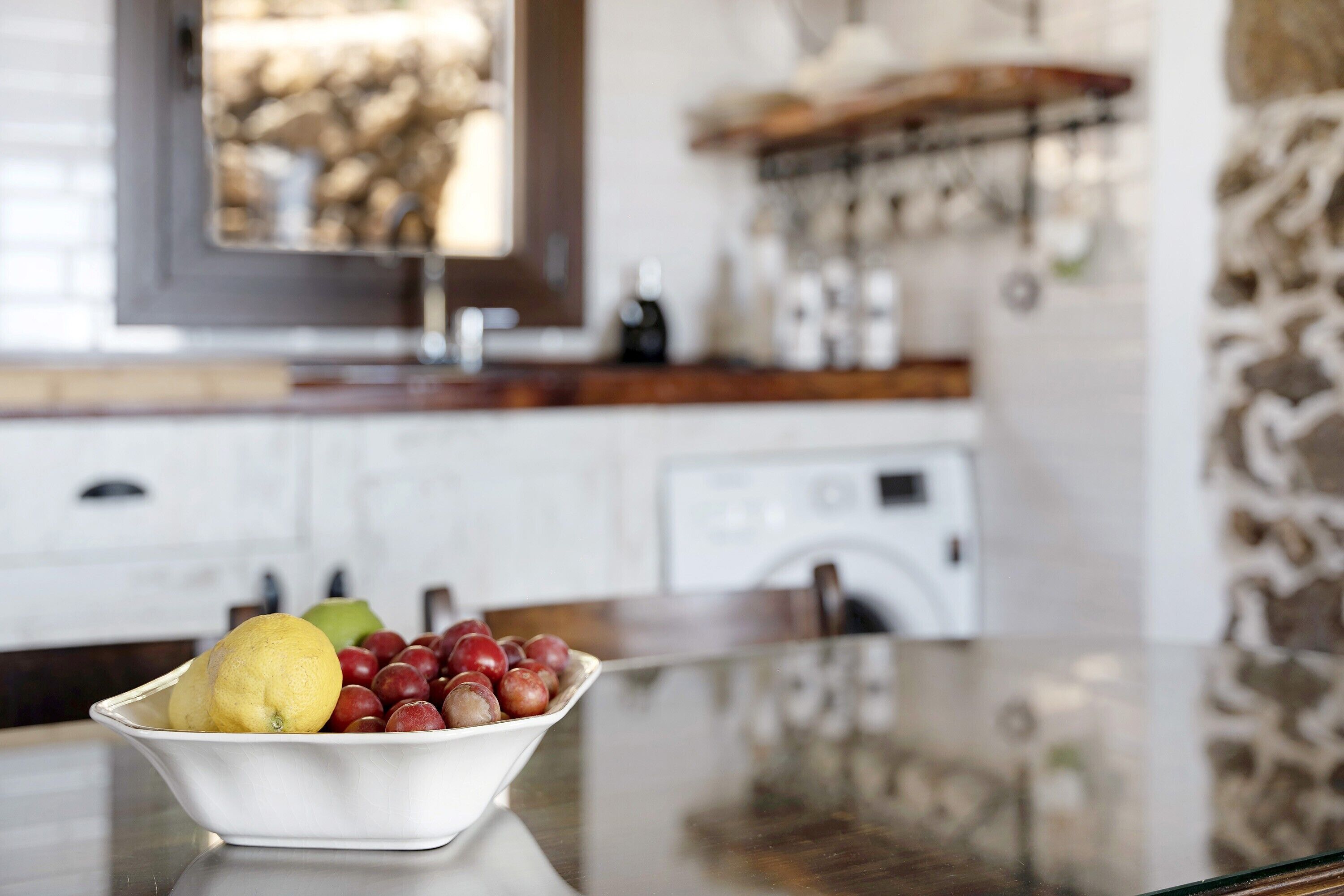 Une cuisine avec un saladier de fruits sur le comptoir, une fenêtre donnant sur des arbres et un appareil électroménager blanc en arrière-plan.
