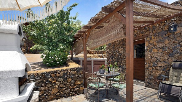 Une terrasse en pierre avec un barbecue, des sièges d’extérieur et une pergola.