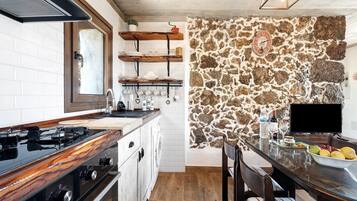 Une cuisine avec un mur en pierre, des étagères en bois, une cuisinière et un coin repas comprenant une table et des chaises.