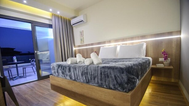 A modern bedroom with a large bed, a wooden headboard, and a view of the outdoors. - Yakinthos Hotel (Katerini)