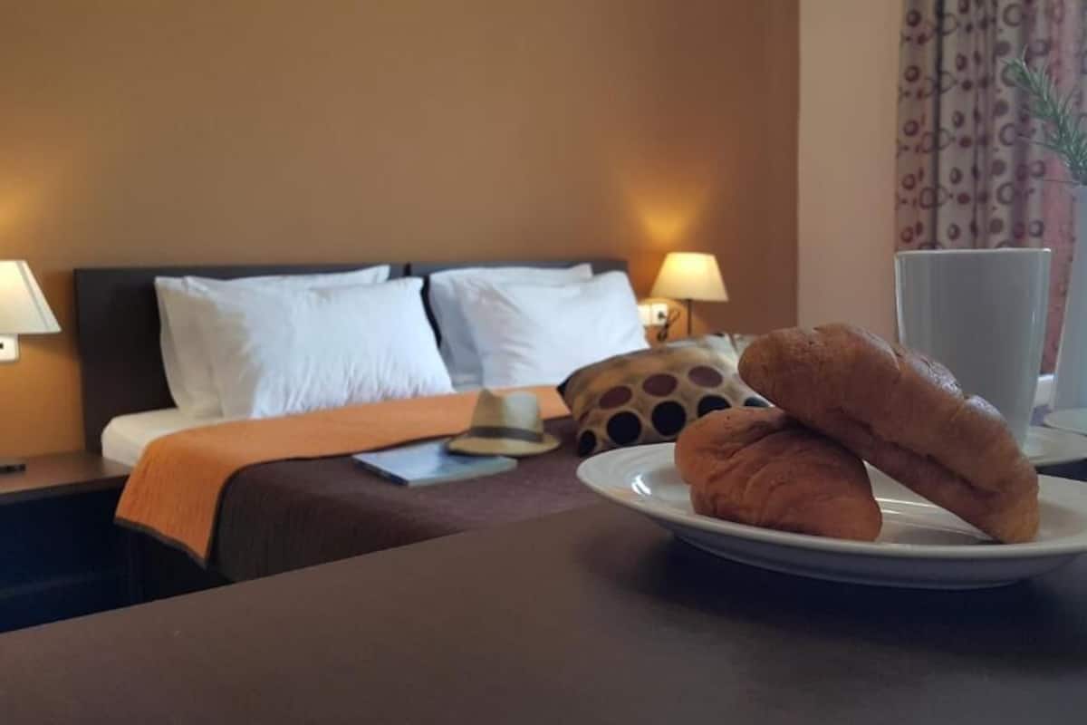 Une chambre d’hôtel avec un lit, des lampes de chevet, une assiette de croissants et un vase rempli de fleurs.