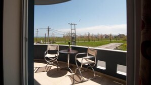 A balcony with two chairs and a small table, overlooking a green field and buildings. - Yakinthos Hotel (Katerini)