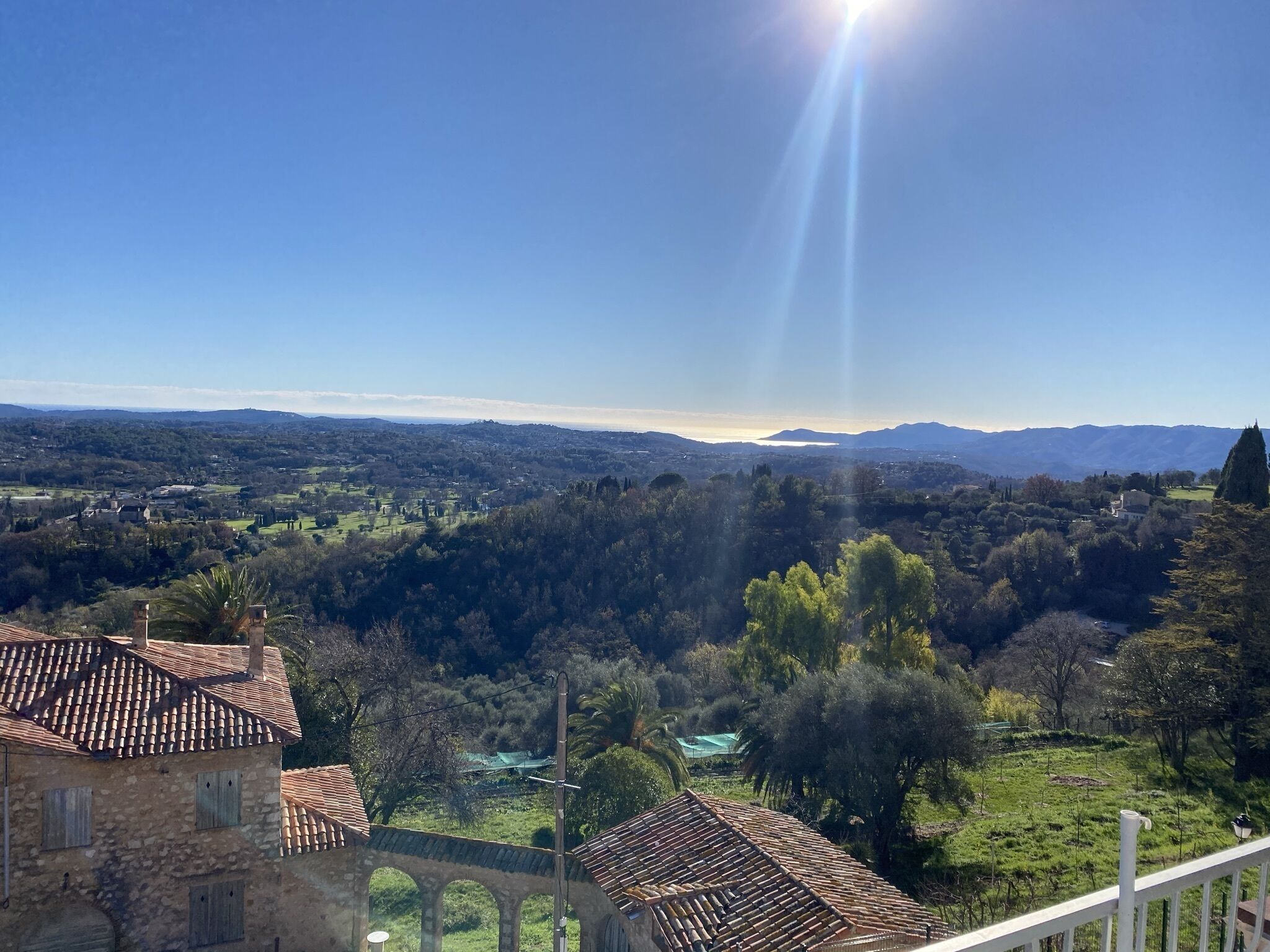 Blick auf eine ländliche Landschaft mit blauem Himmel, entfernten Bergen und einem traditionellen Steinhaus mit Ziegeldach.