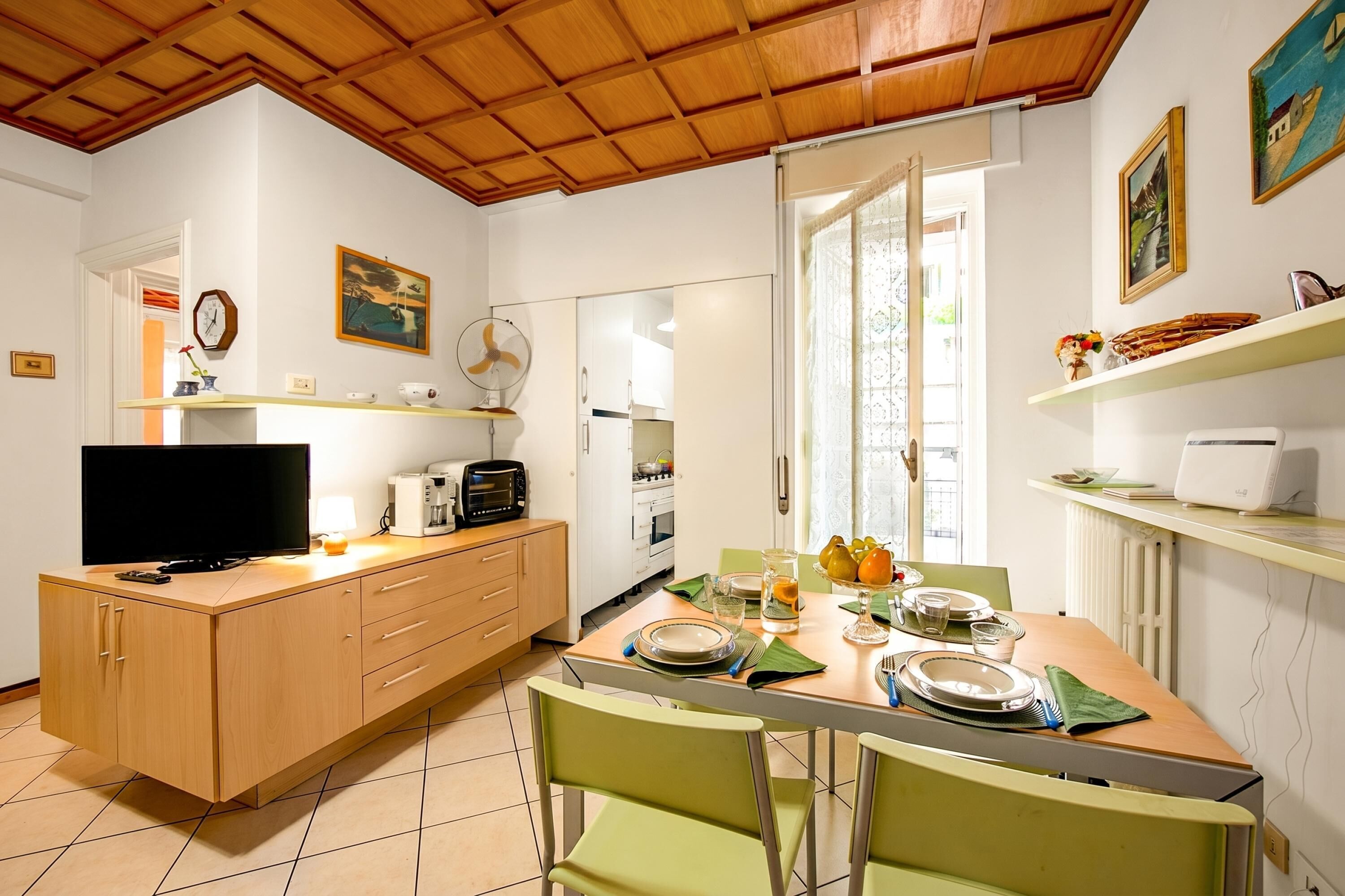 A kitchen with a TV, a fan, and a dining table set for four with plates and glasses.