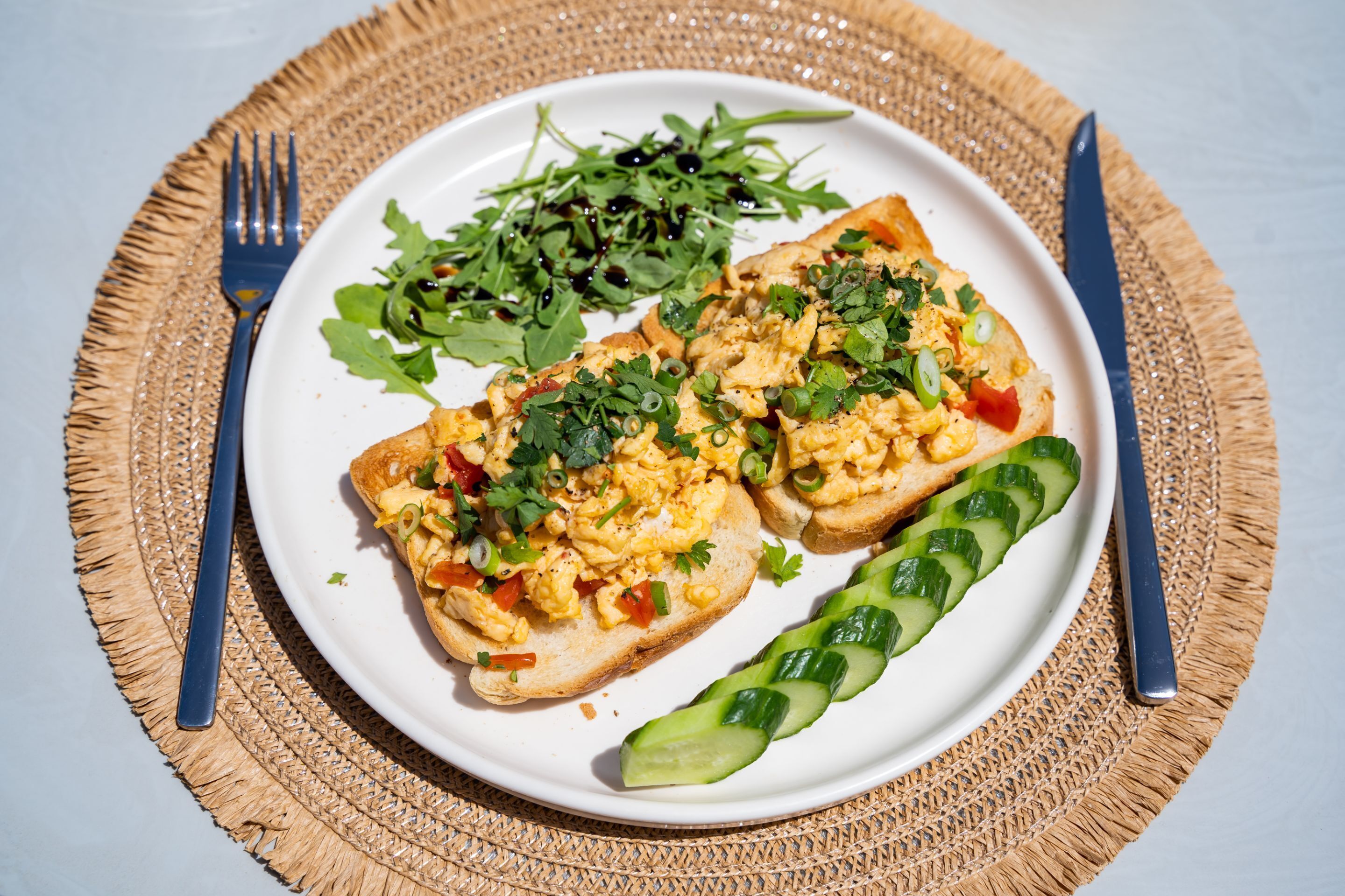 A plate with scrambled eggs on toast, a side salad, and cucumber slices.