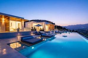 A modern infinity pool with lounge chairs and a glass-enclosed patio area.