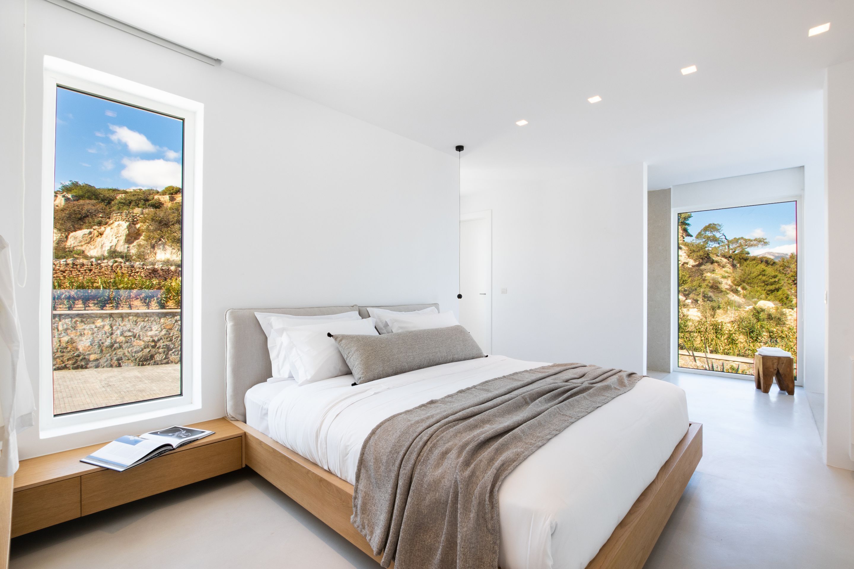 Ein modernes Schlafzimmer mit einem großen Bett, integrierten Nachttischen und Blick auf eine felsige Landschaft durch große Fenster.
