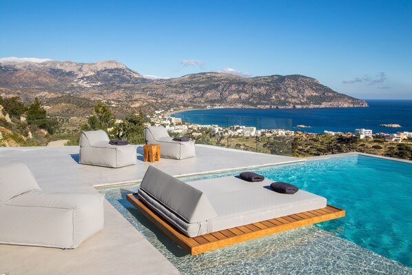 A poolside area with lounge chairs and a view of the sea and mountains. - Istia Luxury Villas (Karpathos)