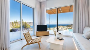 A modern living room with a large TV, a wooden chair, a white sofa, and a coffee table. - Istia Luxury Villas (Karpathos)