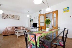 Ein Wohnzimmer mit einer Couch, einem Esstisch mit Glasplatte und einem Fernseher.