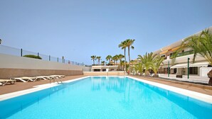 Una piscina con lettini, palme e un edificio con balconi.