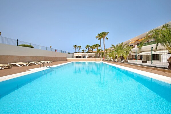 A swimming pool with lounge chairs, palm trees, and a building with balconies.