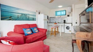 Un ambiente compatto con un divano rosso, angolo cottura, lavatrice e ventilatore a soffitto.