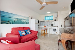 A compact living space with a red sofa, a kitchen area, a washing machine, and a ceiling fan.