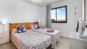 Camera da letto con due letti, una finestra, una ventola a soffitto e un comodino.