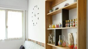 Ein Zimmer mit einem Holzbodenregal, das verschiedene Gegenstände, eine Wanduhr und ein Fenster mit Vorhängen beherbergt.