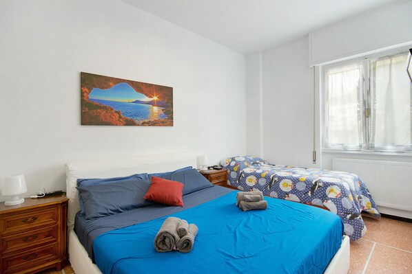 A bedroom with a bed, a nightstand, a bedside table, a window, and a painting on the wall.