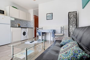 Une cuisine moderne équipée d’un lave-linge, un coin repas avec une table et des chaises, et un salon avec un canapé et des coussins.