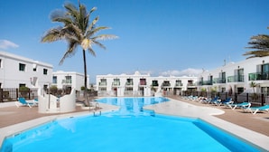 Ein Pool mit Liegestühlen, Palmen und weißen Gebäuden mit Balkonen.