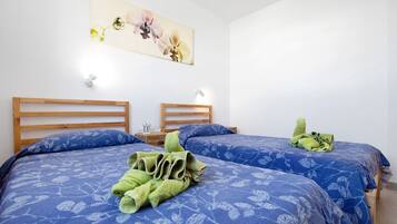 Habitación de hotel con dos camas, cada una con colcha azul estampada con flores, cabecero de madera y mesita de noche con lámpara.