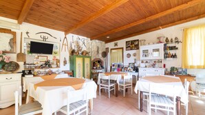 A rustic dining area with wooden beams, white tables, and chairs. - Holiday Home 'Fattoria Spezia - Nespola' with Shared Pool, Garden and Shared Wi-Fi (Buseto Palizzolo)