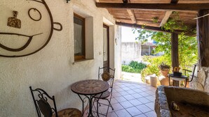 A patio with a tiled floor, a round table, two chairs, a decorative wall with a face, and a wooden ceiling. - Holiday Home 'Fattoria Spezia - Nespola' with Shared Pool, Garden and Shared Wi-Fi (Buseto Palizzolo)
