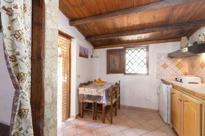 A kitchen with a wooden ceiling, a dining table with chairs, a refrigerator, and a window with a view.