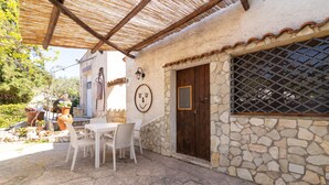 A stone building with a wooden door, a window with a metal grid, and a white table with chairs outside. - Holiday Home 'Fattoria Spezia - Limone' with Shared Pool, Shared Garden and Wi-Fi (Buseto Palizzolo)