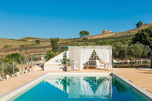A pool area with a white gazebo, a stone wall, and a view of hills.