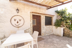A patio with a white table and chairs, a stone wall, a wooden door, and a window with a metal grill.