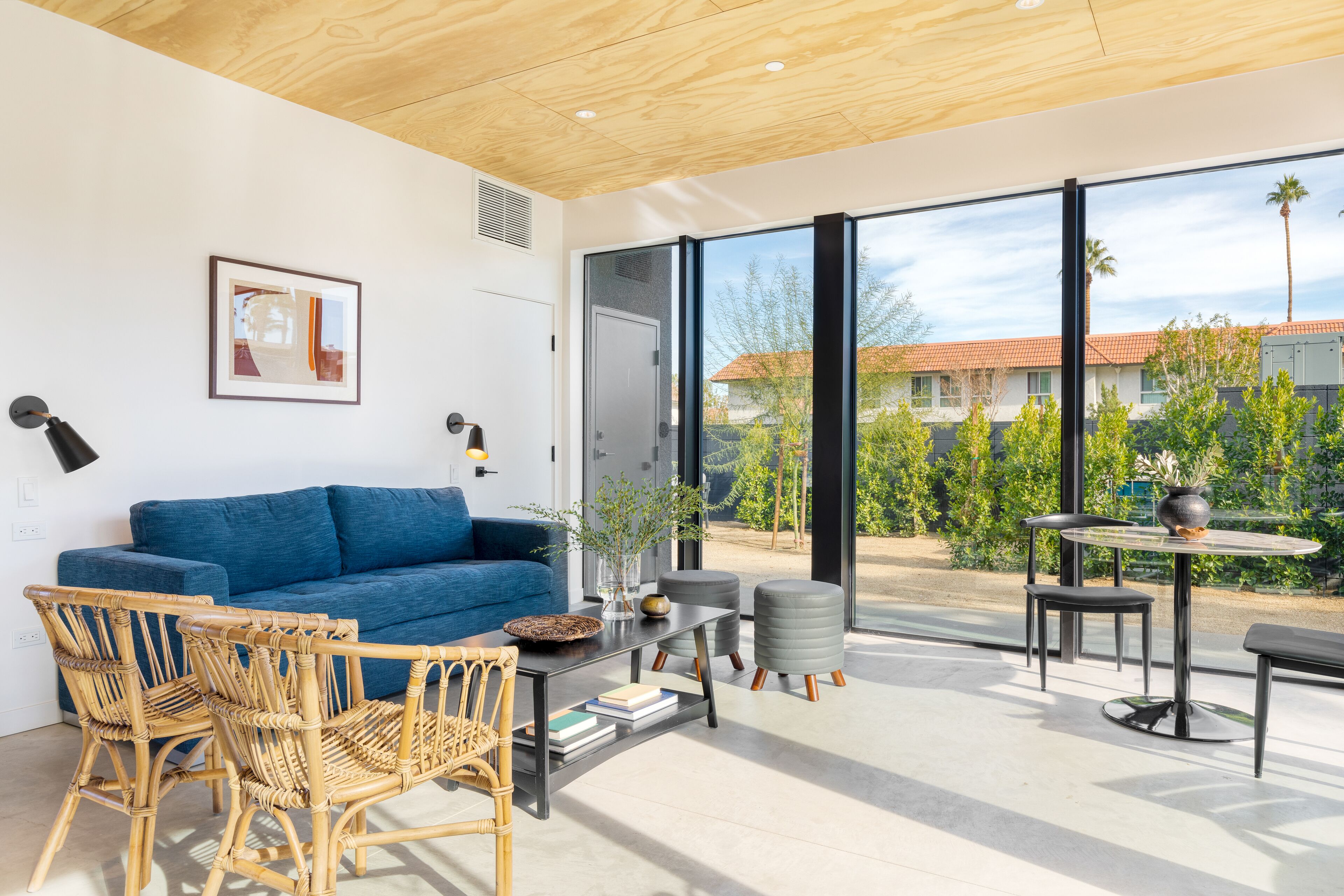 A modern living room with a blue sofa, wicker chairs, a coffee table, and a view of the outside.