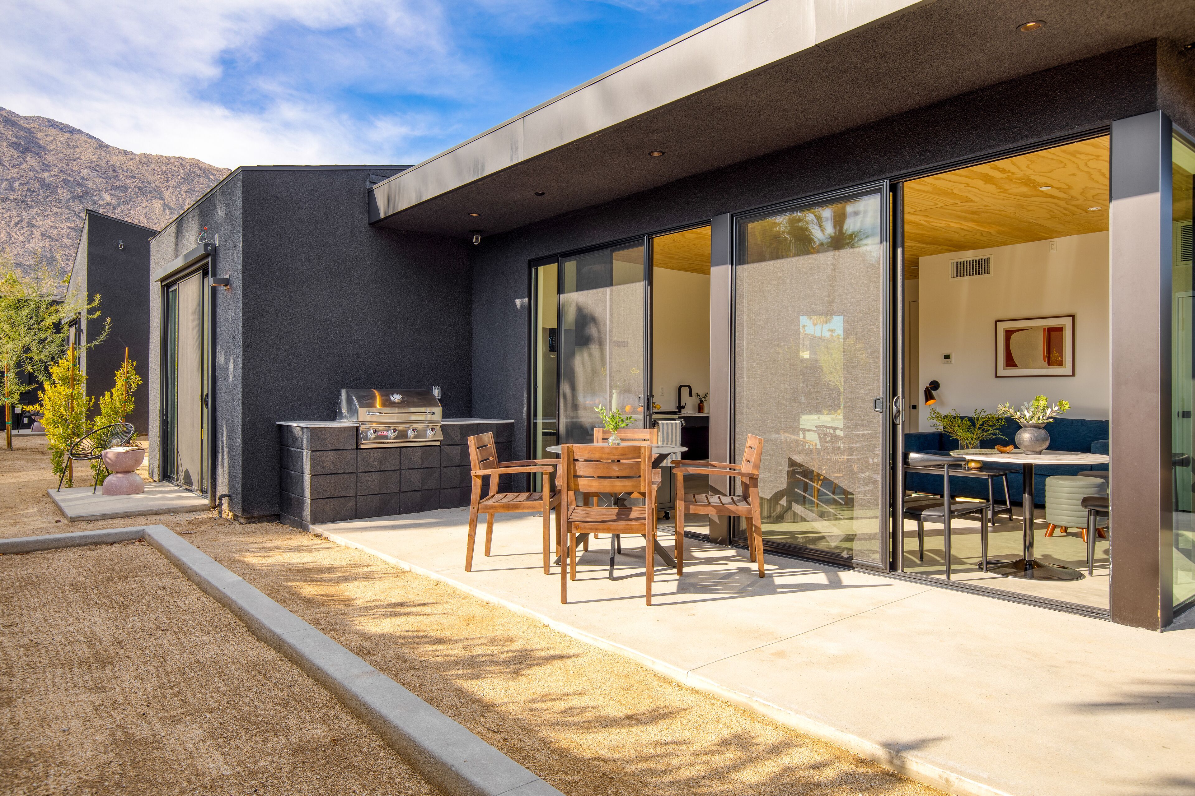 A modern house with a patio, a grill, and a dining area with chairs and a table.