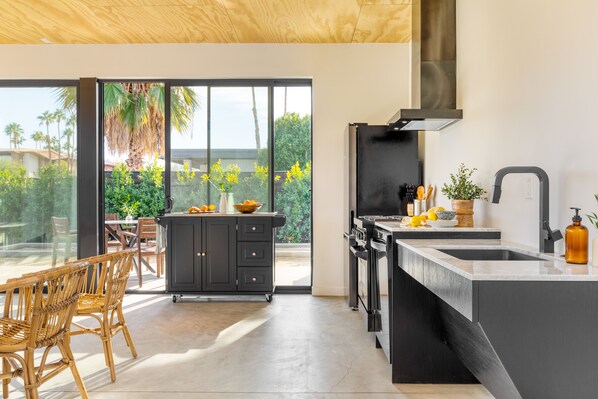 Cocina moderna con una isla grande, armarios negros y vistas a un patio con mobiliario exterior.