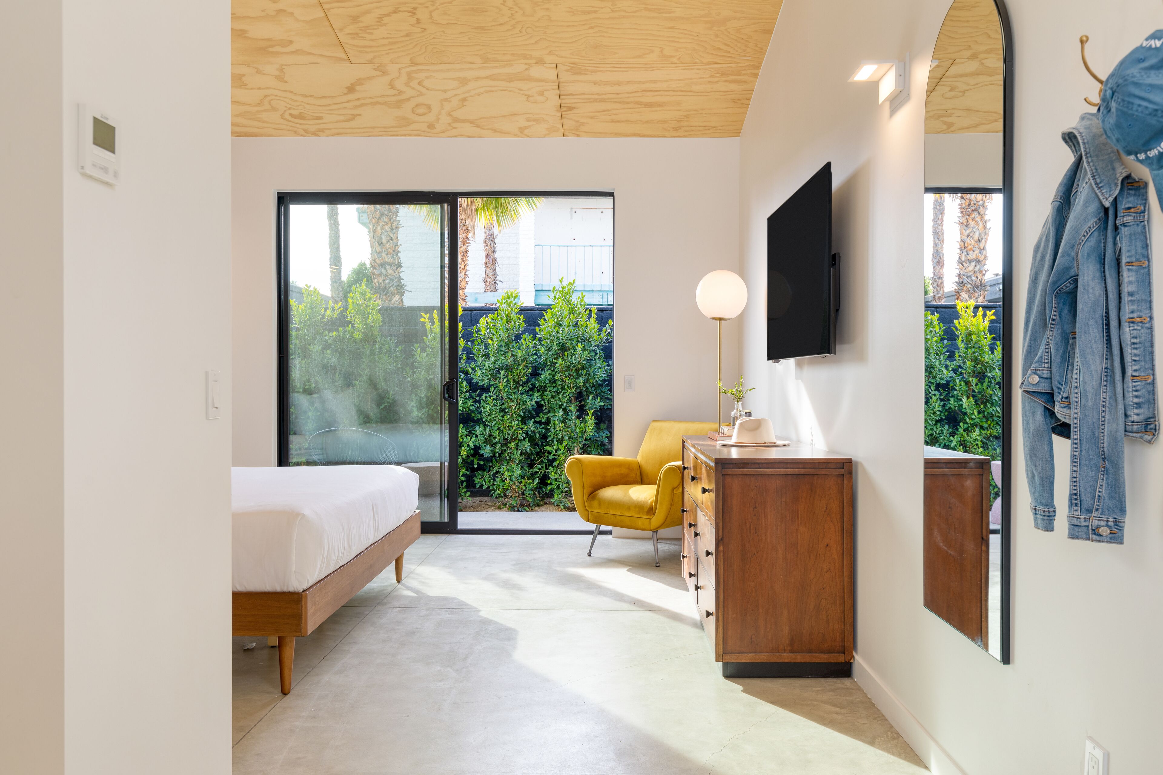 Una camera da letto moderna con un letto, una poltrona gialla, una cassettiera in legno e una TV fissata al muro.