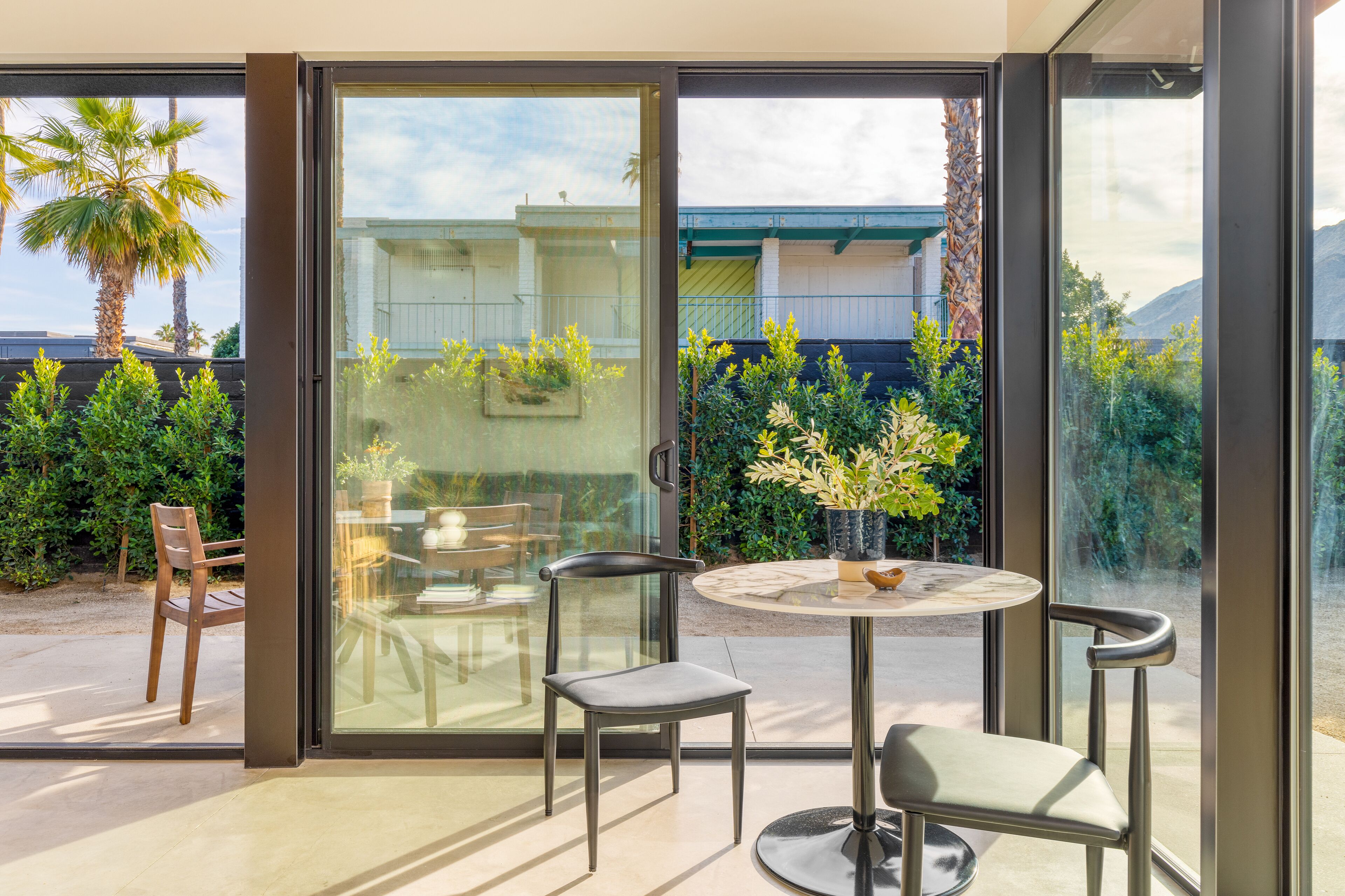 A modern patio with a glass door leading to a garden, featuring a round table and two chairs.