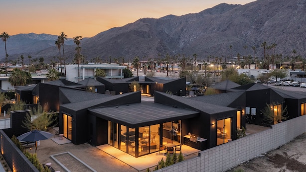 Un resort moderno con varias edificaciones de techo negro, un patio central abierto y palmeras.