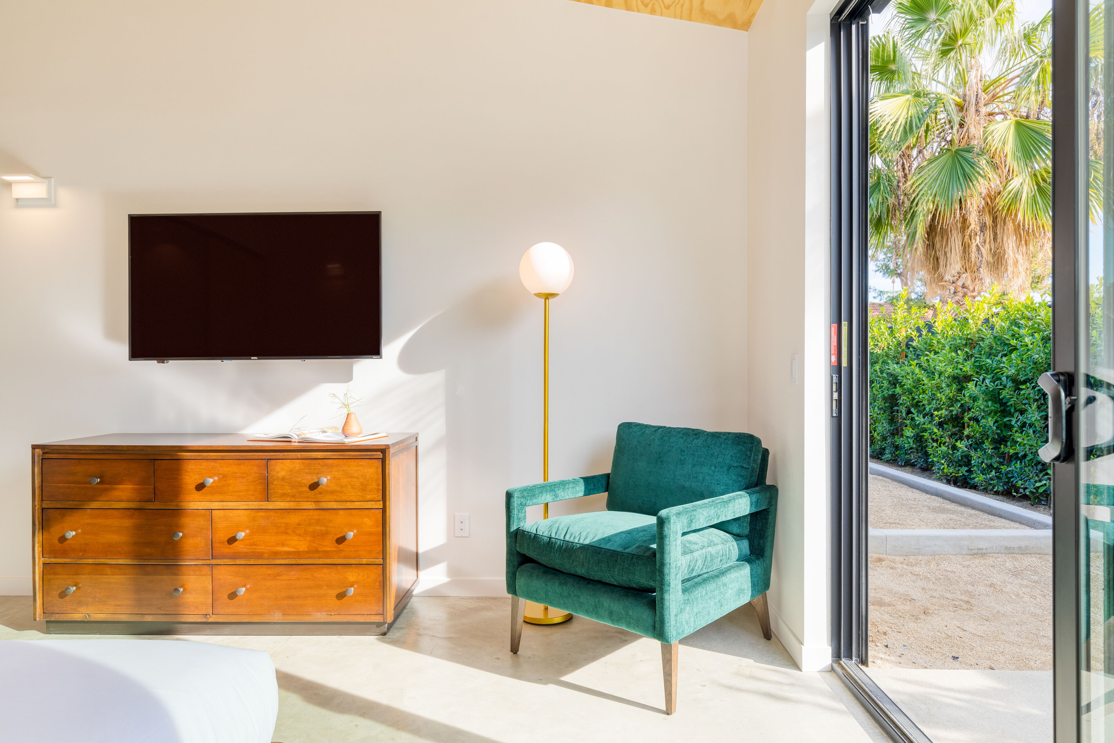 A modern living room with a wooden dresser, a teal armchair, and a floor lamp.