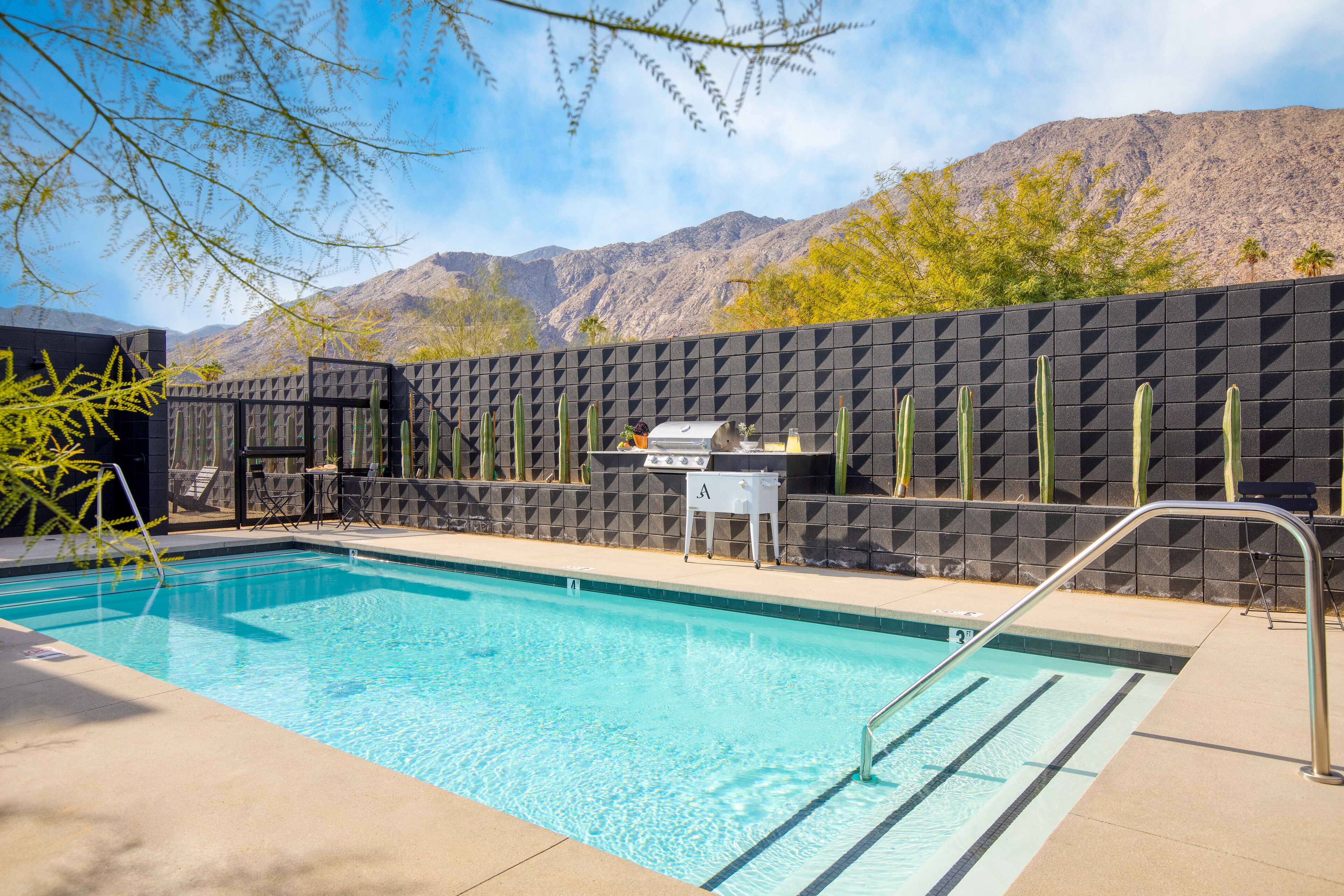 A swimming pool with a black textured wall, a grill, and chairs.