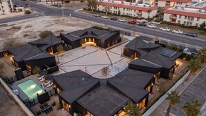 A modern hotel with multiple black-roofed buildings, a swimming pool, and a parking lot.