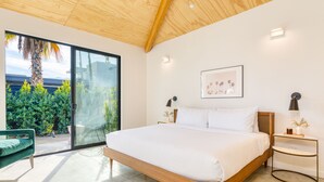 Ein modernes Schlafzimmer mit einem großen Bett, einer Schiebetür zu einem Balkon und Blick ins Grüne.