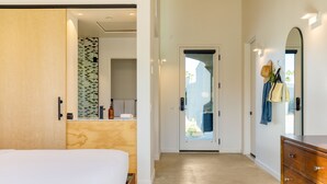 Ein Hotelzimmer mit einem Bett, einer Holzkommode, einem Spiegel und einem durch eine offene Tür einsehbaren Badezimmer.